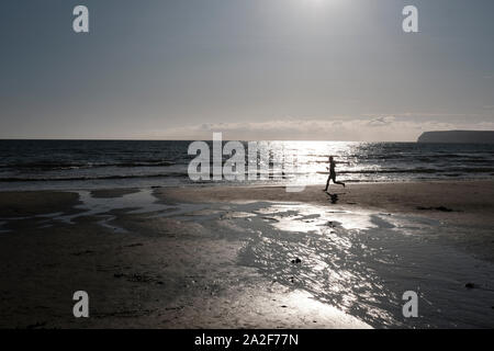 Ein Mann entlang der flachen sandigen Küste von Compton Strand bei Ebbe läuft am späten Nachmittag Sommer Sonnenschein Stockfoto