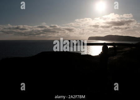 Durchführung Surfboard auf dem Kopf ein Surfer Köpfe in Silhouette über die Klippen in Compton Chine auf der Isle of Wight Stockfoto