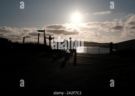 Durchführung Surfboard auf dem Kopf ein Surfer Köpfe in Silhouette über die Klippen in Compton Chine auf der Isle of Wight Stockfoto