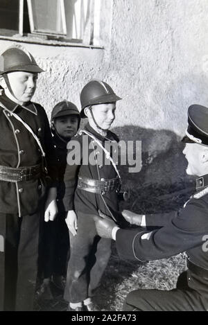 Ein Feuerwehrmann überprüft bei einer Übung der Kinderfeuerwehr ob Uniform eines Jungen richtig sitzt, Deutschland 1930er Jahre. Ein Feuerwehrmann ist die Überprüfung der rechte Sitz der Einheitlichen eines Jungen während eines Trainings der Junior Feuerwehrmänner, Deutschland 1930. Stockfoto