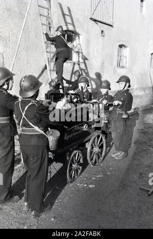 Eine Gruppe von der Kinderfeuerwehr mit dem Löschwagen und der Projektleiter bei einer Feuerwehrübung, Deutschland 1930er Jahre. Eine Gruppe von Junior Feuerwehrmänner ist die Vorbereitung der firewagon und Leiter während ein Feuerwehrmann, Deutschland 1930. Stockfoto