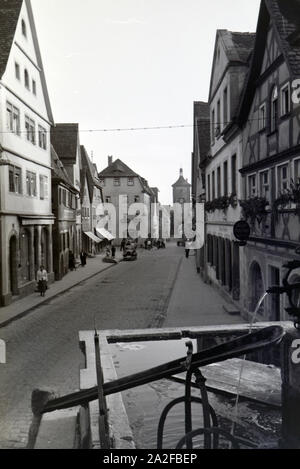 Eine von Fachwerkhäusern gesäumte Straße mit einem Springbrunnen in Rothenburg o.d. Tauber, Deutschland 1930er Jahre. Eine Straße mit Fachwerkhäusern und einem Brunnen in Rothenburg o.d. Tauber, Deutschland 1930 gesäumt. Stockfoto