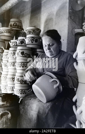 Eine Töpfermeisterin aus dem Kannenbäckerland bemalt Steinkrüge in der charakteristischen blauen Glasur des Westerwälder Steinguts, Deutschland 1930er Jahre. Ein Master Potter Malerei steinzeug Krüge in der typischen blauen Farbe der Westerwälder Steinzeug, Deutschland 1930. Stockfoto