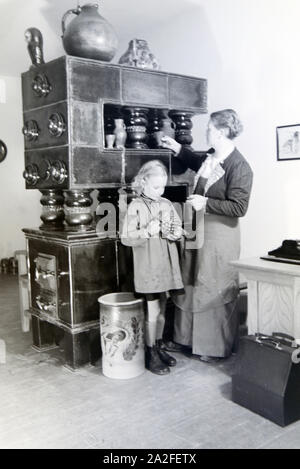 Eine Töpfermeisterin aus dem Kannenbäckerland zeigt einem kleinen Mädchen einen fertig gebrannten Tonkrug, Deutschland 1930er Jahre. Ein Master Potter zeigt eine fertige Steinzeug Krug zu einem kleinen Mädchen, Deutschland 1930. Stockfoto