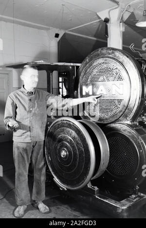 Ein Arbeiter posiert vor einer Rotationsdruckmaschine in den Werken des Maschinenbaukonzerns MAN (Maschinenfabrik Augsburg-Nürnberg), Deutschland 1930er Jahre. Ein Arbeitnehmer vor einer Rotationsdruckmaschine posieren in den Anlagen der mechanischen Engineering Company MAN (Maschinenfabrik Augsburg-Nürnberg), Deutschland 1930. Stockfoto