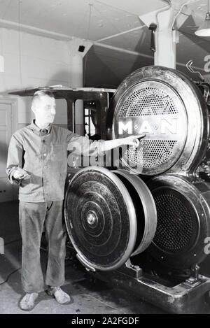 Ein Arbeiter posiert vor einer Rotationsdruckmaschine in den Werken des Maschinenbaukonzerns MAN (Maschinenfabrik Augsburg-Nürnberg), Deutschland 1930er Jahre. Ein Arbeitnehmer vor einer Rotationsdruckmaschine posieren in den Anlagen der mechanischen Engineering Company MAN (Maschinenfabrik Augsburg-Nürnberg), Deutschland 1930. Stockfoto