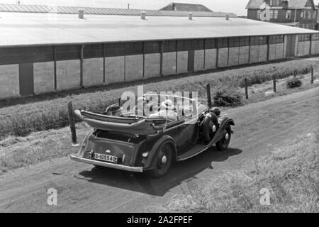 Unterwegs in einem Audi Cabrio zu den Garagen in Norddeich, Deutschland 1930er Jahre. Menschen in einem Audi Cabrio zu den Garagen bei Norddeich, Deutschland 1930. Stockfoto