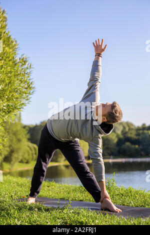 Man Yoga Asanas im City Park inspiriert. Fitness im Freien und Life Balance Konzept. Stretching. Dreieck Pose oder Trikonasana Stockfoto