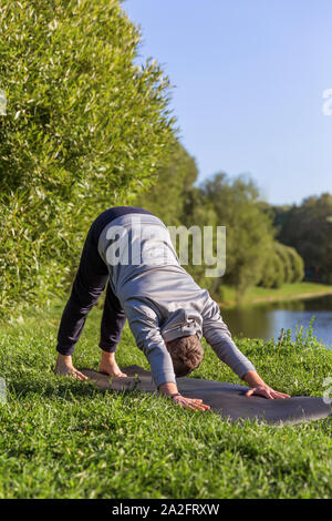 Man Yoga Asanas im City Park inspiriert. Fitness im Freien und Life Balance Konzept. In den nach unten schauenden Hund Pose oder Adho Mukha shvanasana Stockfoto