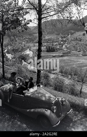 Ein junges Paar und ihr Hund bei einer Spazierfahrt mit dem Mercedes Cabrio in Hirsau im Nordschwarzwald, Deutschland 1930er Jahre. Ein junges Paar und ihr Hund fahren durch Hirsau im Nordschwarzwald in einem Mercedes Cabrio, Deutschland 1930. Stockfoto