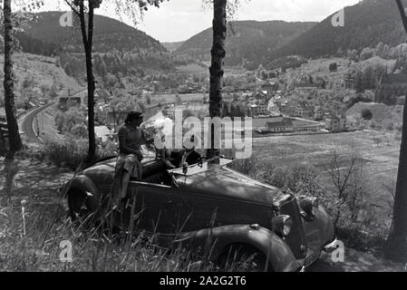 Ein junges Paar und ihr Hund bei einer Spazierfahrt mit dem Mercedes Cabrio in Hirsau im Nordschwarzwald, Deutschland 1930er Jahre. Ein junges Paar und ihr Hund fahren durch Hirsau im Nordschwarzwald in einem Mercedes Cabrio, Deutschland 1930. Stockfoto