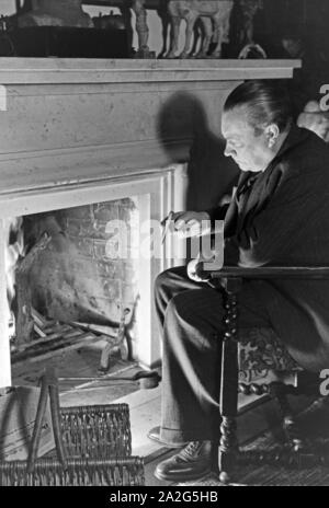 Der deutsche Mass Paul Wegener sitzt zu Hause am Kamin und raucht eine Zigarre in Berlin, Deutschland, 1930er Jahre. Deutsche Schauspieler Paul Wegener Zigarre während am Kamin in seinem Haus in Berlin sitzen, Deutschland 1930. Stockfoto