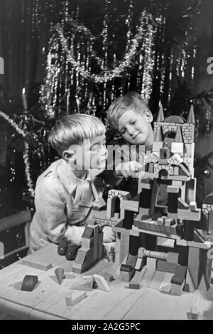 Zwei Jungen spielen am Weihnachtsabend mit den neuen Bauklötzen, Deutschland 1938. Zwei Jungs spielen mit der neuen Spielzeug Bausteine unter dem Weihnachtsbaum, Deutschland 1930 Stockfoto