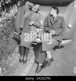 Eine junge Frau und ein junger Mann entspannen sich auf der Kofferraummhaube eine Opel Admiral, Deutschland 1930er Jahre. Ein junges Paar entspannen auf dem Boot von einem Opel Modell Admiral, Deutschland 1930. Stockfoto