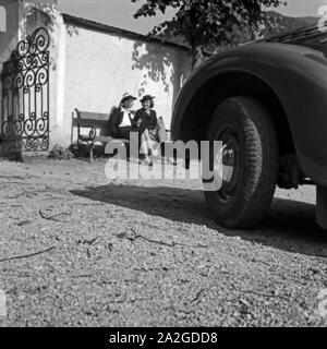 Zwei Frauen Artikel vor einem Eingangstor in einer Bank, davor der geparkte Opel Olympia, Österreich 1930er Jahre. Zwei Frauen auf einer Bank vor einem Eingang, einem geparkten Opel Olympia vor Ihnen, Österreich, 1930. Stockfoto