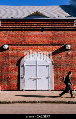 Dez 2, 2018 Hakodate, Japan - Weiß Eisentor mit Red brick wall alten rustikalen Industrielle loft Retro Vintage Lager Wand mit Menschen zu Fuß auf sidew Stockfoto