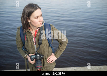 Nachdenkliche Frau Fotograf mit der Kamera in der Hand auf dem Hintergrund des Flusses und in die Ferne schaut. Stockfoto