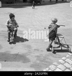 Zwei Kinder Spielen Mit Einem Dreirad, 1930er Jahre Deutschland. Zwei Kinder spielen mit einem Dreirad, Deutschland der 1930er Jahre. Stockfoto