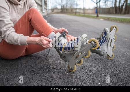 Mädchen sitzen auf der Straße und das Binden der Schnürsenkel auf Rollschuhen, close-up. Konzept: Sport, gesunde Lebensweise. Stockfoto