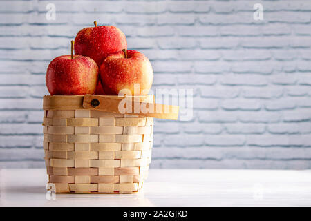 Äpfel in einem Korb auf einem weißen Tisch mit einem weißen Stein Wand Stockfoto