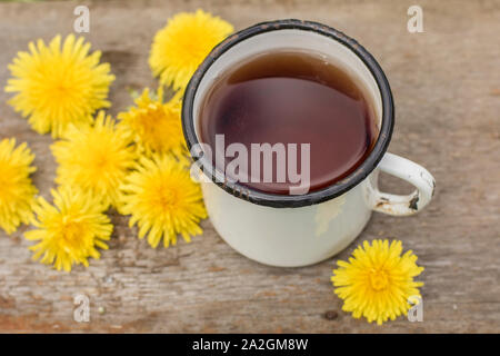 Tee aus gelben Blumen Löwenzahn (Taraxacum officinale) in einem weiß emaillierte alte Schale, eine Feder, warmen Tag. Stockfoto