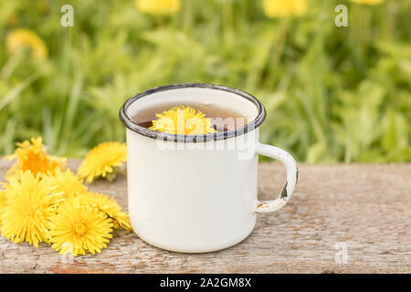 Tee aus gelben Blumen Löwenzahn (Taraxacum officinale) in einem weiß emaillierte alte Schale, eine Feder, warmen Tag. Stockfoto