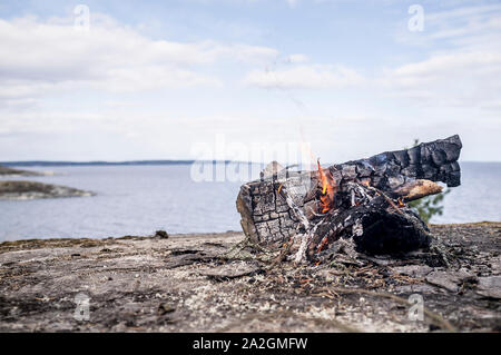 Lagerfeuer an der felsigen Ufer des Sees, vor dem Hintergrund der Himmel und Wolken, an einem Frühlingstag. Stockfoto