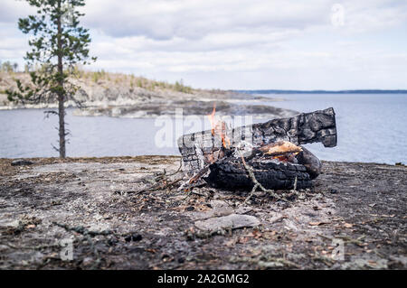 Lagerfeuer an der felsigen Ufer des Sees, vor dem Hintergrund der einsame Kiefer und Sky, an einem Frühlingstag. Stockfoto