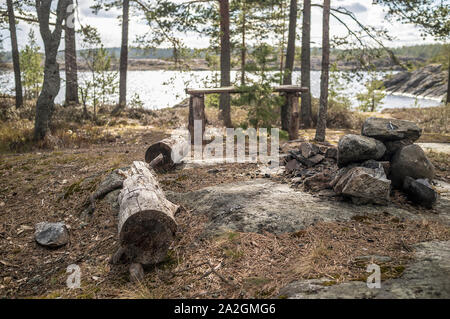 Camp auf dem felsigen Ufer des Sees. Einer alten hölzernen Tisch, eine Bank von Logs und ein Platz für ein Feuer unter den Kiefern. Stockfoto