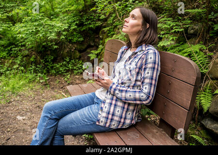 Schöne Frau sitzt auf einer Holzbank in der Forest Park in der Nähe der Trail, der in seinen Händen ein Notizbuch und Bleistift, verträumt in den Himmel starrte. Stockfoto