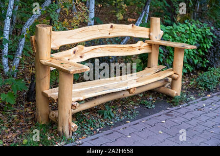 Schöne neue Bank aus Holz der Zeder steht im Park auf einem Hintergrund von grünen Bäumen, Stockfoto