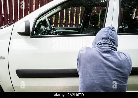 Ein Mann - ein Dieb in ein Sweatshirt mit Kapuze versuchen, ein Auto zu stehlen und ein Schloss brechen Stockfoto