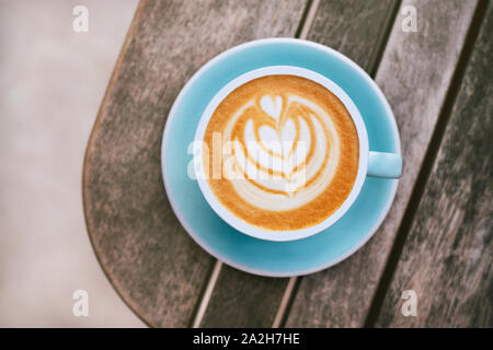 Cappuccino mit aufgeschäumter Schaumstoff, blau Kaffeetasse obere Ansicht Nahaufnahme auf grau Holz- Hintergrund. Flach Stil. Stockfoto