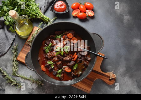 Rindfleisch Bourguignon in einer Pfanne. Eintopf mit Rotwein, Karotten, Zwiebeln, Knoblauch, einem Bouquet garni, und garniert mit Perlzwiebeln, Champignons und Speck. Stockfoto