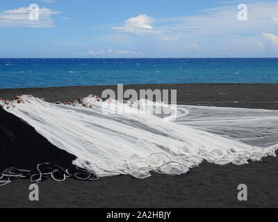 Schwarze und weiße Fischernetze trocknen auf dem schwarzen Sand am Strand auf La Réunion, Frankreich Stockfoto