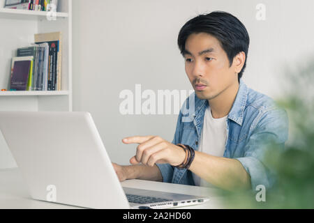 Jungen asiatischen Casual Geschäftsmann, Laptop Monitor am Arbeitsplatz im Büro zu Hause. Zwanglose geschäftliche oder private Unternehmen im Home Office Stockfoto