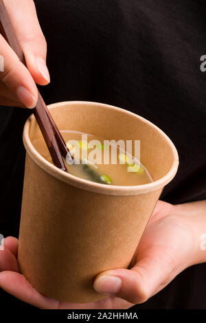 Miso Suppe mit Tofu und Algen im Takeaway Cup. Schöne Frau Essen unterwegs. Stockfoto