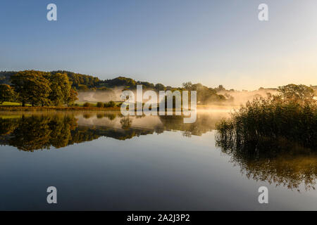 Reflexionen über Esthwaite Wasser als Herbst Nebel löscht und die Sonne bricht durch Stockfoto