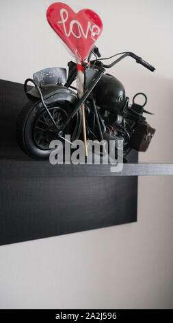 Metall Motorrad Spielzeug Modell auf einem Holzregal mit einem Lutscher in der Form eines Herzens Stockfoto