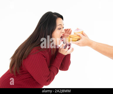 Eine junge fette Frau in Rot gekleidet war Essen einen Hamburger und Krapfen, die übergeben wurde. Sie ist hungrig und ihr Lieblingsessen. Gesundes Konzept. Stockfoto