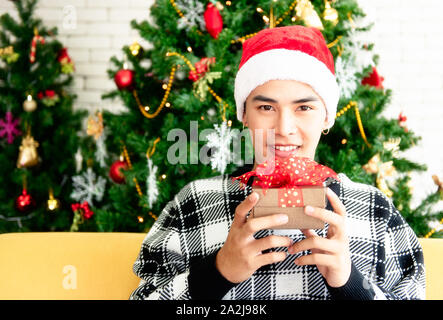 Ein junger Mann, der eine Santa mit einem Weihnachtsbaum auf der Rückseite. Er lächelte und war froh, eine Box Weihnachten Geschenk von seiner Freundin zu bekommen. Close Up und c Stockfoto