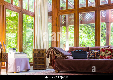 Offene Wohn Ort Zimmer mit alten Sofa, rustikale Brust und große französische Fenster, grüne Bäume im Garten suchen, Lőverek, Sopron, Ungarn Stockfoto