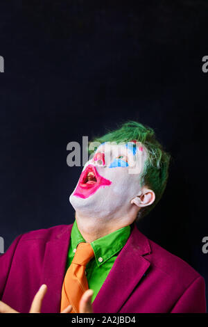 Mann in Mime makeup Cosplay mit grünen Haaren und einem roten Anzug eine orangefarbene Krawatte und ein grünes T-Shirt. Stockfoto