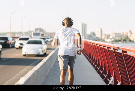 Sportliche schwarze Kerl entlang der Brücke läuft Stockfoto