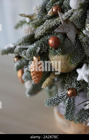 Weihnachtsschmuck auf dem kleinen Weihnachtsbaum. Künstlicher Schnee auf Tanne, Weihnachten Kugeln und Sterne. Konzept der Feiertage des neuen Jahres und Dekorationen Stockfoto