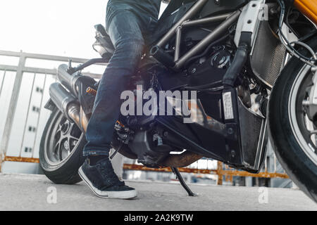 In der Nähe von biker Turnschuhe tragen und sitzen auf dem Motorrad am Parkplatz. Stockfoto