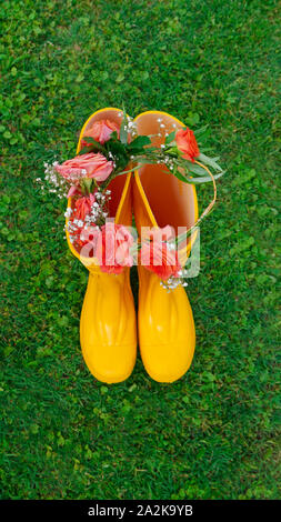 Gelbe Gummistiefel mit Kranz von Orange Rosen auf grünem Gras Stockfoto