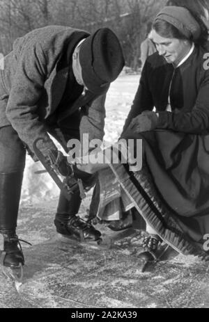 Mein Mann hilft einer Frau beim Anschnallen von Schlittschuhkufen im Spreewald, Deutschland, 1930er Jahre. Ein Mann, eine Frau auf schlittschuh Läufer im Spreewald, Deutschland 1930. Stockfoto