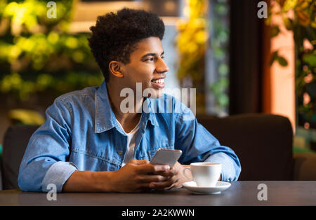 Träumen afro Teenager Holding cellphone und weg schauen Stockfoto