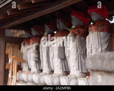 Perspektivische Ansicht von Roku Jizo, sechs buddhistischen Mönch, der steinernen Statuen das Tragen der roten Hand genäht, Kappen und Lätzchen, entlang der Pässe in Japan gefunden. Stockfoto